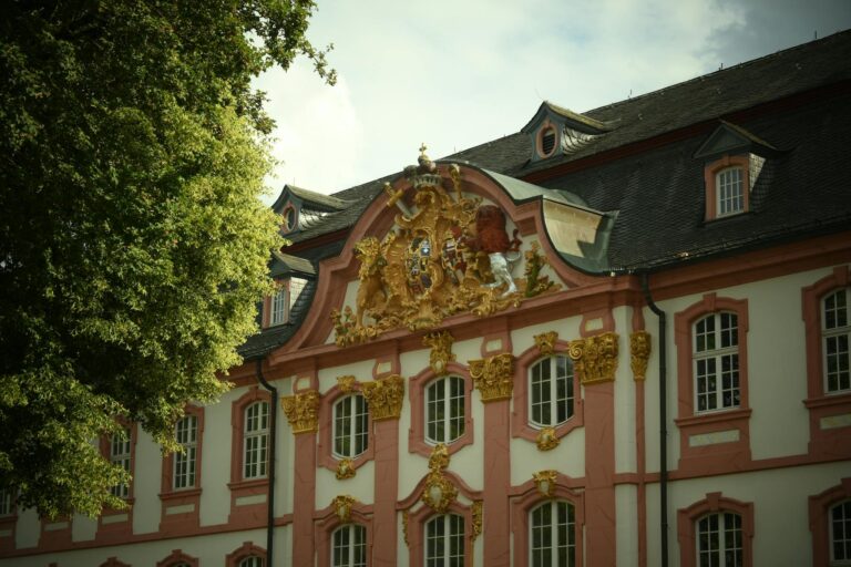 Neoclassical palace facade featuring an ornate emblem on a bright, sunny day.